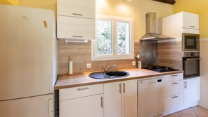 Une cuisine moderne avec des meubles blancs, une cuisinière en acier inoxydable et une fenêtre donnant sur un paysage verdoyant.