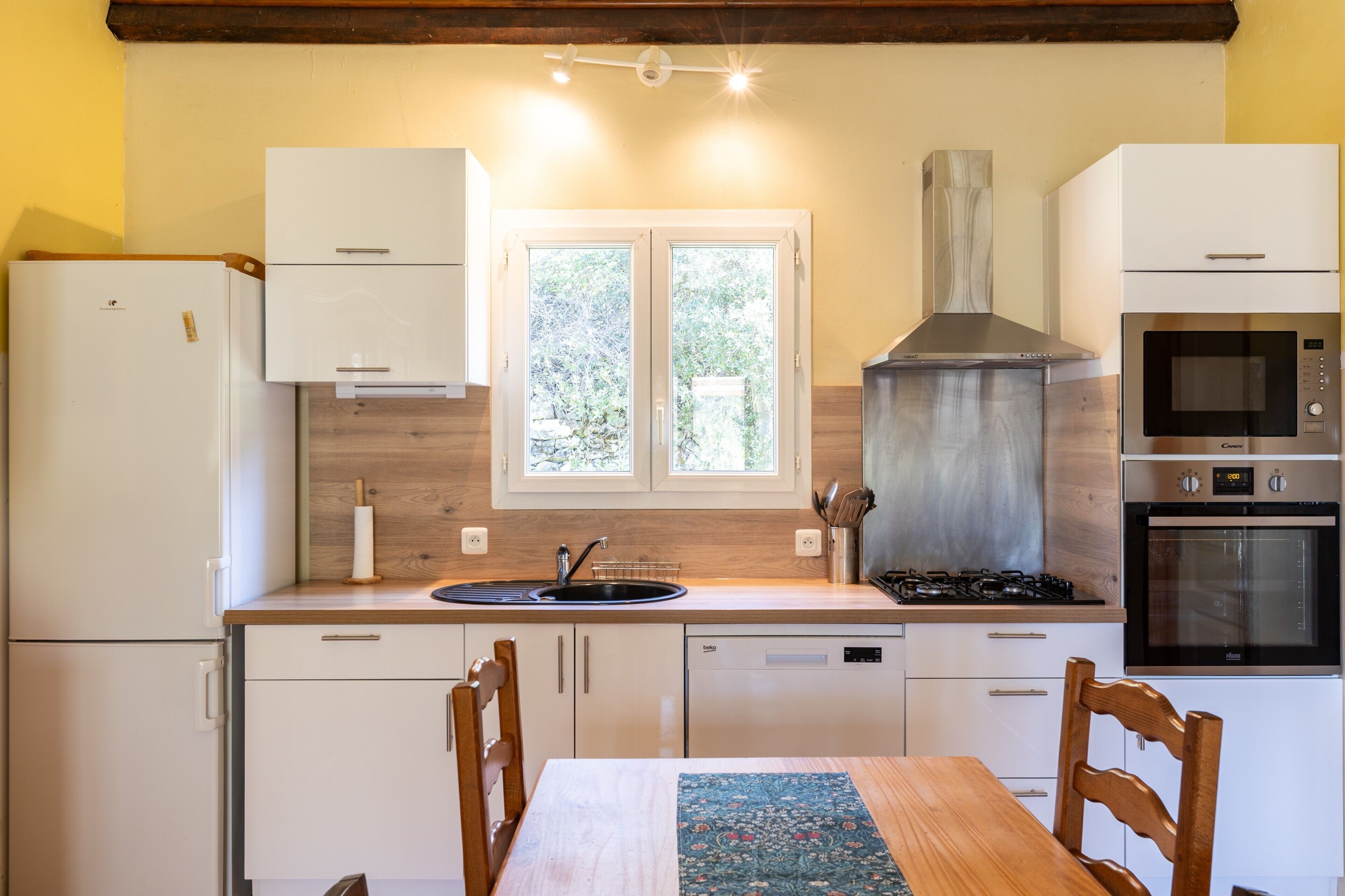 A compact kitchen with a sink, stove, oven, and a window with a view of greenery.