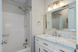 Un baño con bañera, lavamanos con espejo y ducha.