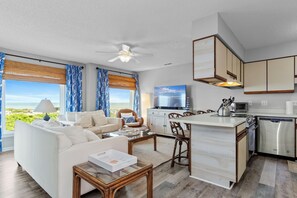 A modern living room with a sofa, coffee table, and a view of the ocean. - Pebble Beach C-308 | Oceanview 3BR Condo w/ Pools & Tennis (Emerald Isle)