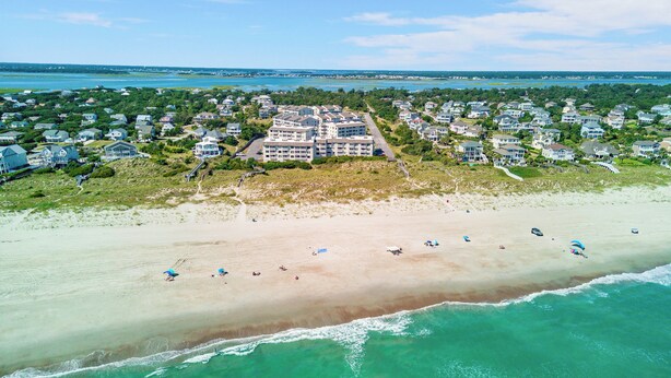 An aerial view of a coastal residential area with houses, a beach, and a large building with multiple floors. - Point Emerald Villa C-106 | Oceanview 2BR Condo w/ Pools, Tennis & Beach Access (Emerald Isle)