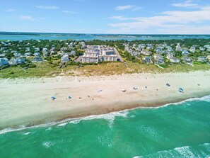 An aerial view of a coastal residential area with houses, a beach, and a large building with multiple floors. - Point Emerald Villa C-106 | Oceanview 2BR Condo w/ Pools, Tennis & Beach Access (Emerald Isle)