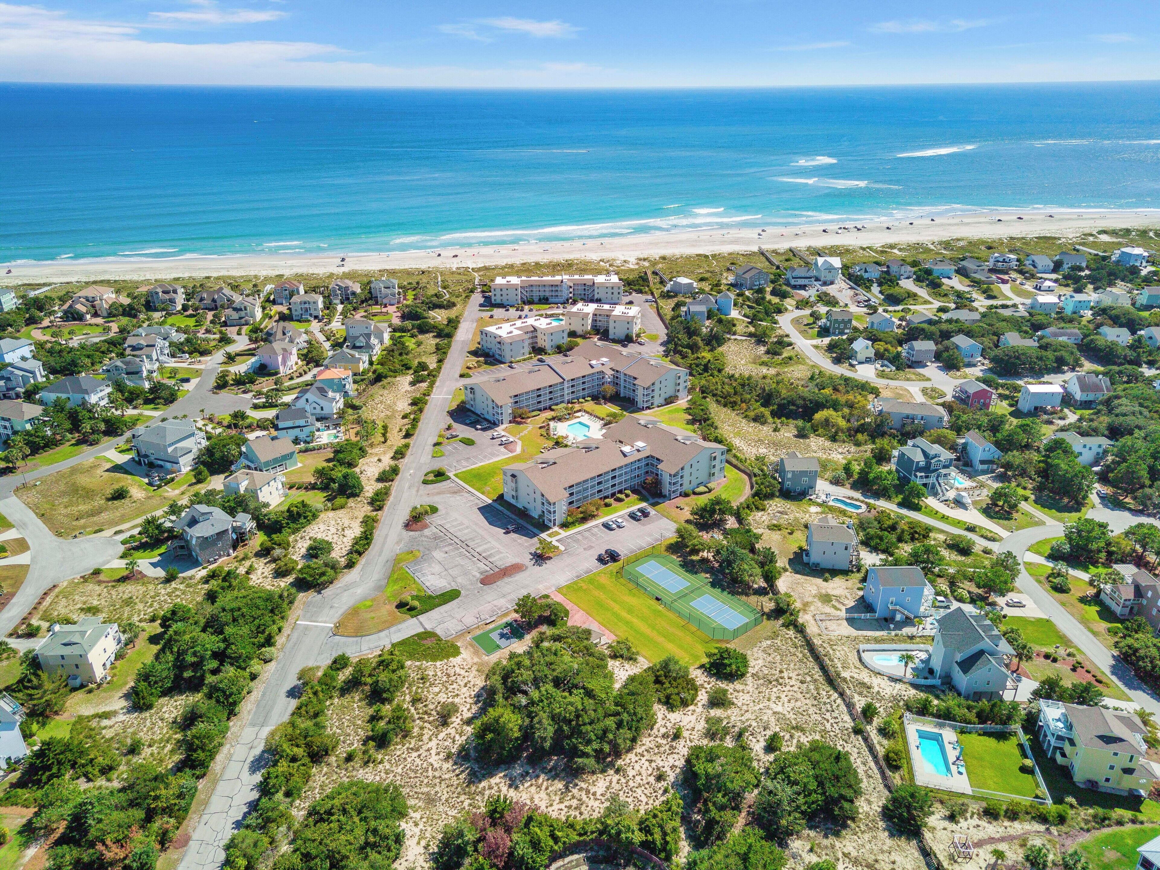 An aerial view of a coastal residential area with houses, a large building complex, and a beach.