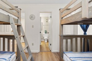 Une pièce avec des lits superposés, une échelle, une horloge et une porte donnant sur une salle de bain.