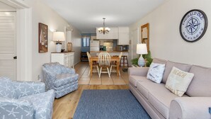 A living room with a sofa, armchair, and dining table with chairs. - Point Emerald Villa C-106 | Oceanview 2BR Condo w/ Pools, Tennis & Beach Access (Emerald Isle)