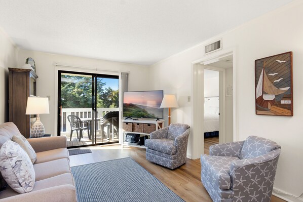 Un salon comprenant un canapé, des fauteuils, un téléviseur et un balcon aménagé avec du mobilier d’extérieur.