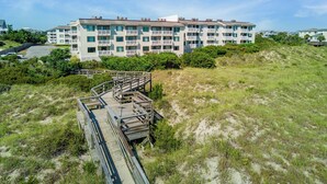 A multi-story building with balconies, a wooden boardwalk, and a grassy area. - Point Emerald Villa C-106 | Oceanview 2BR Condo w/ Pools, Tennis & Beach Access (Emerald Isle)