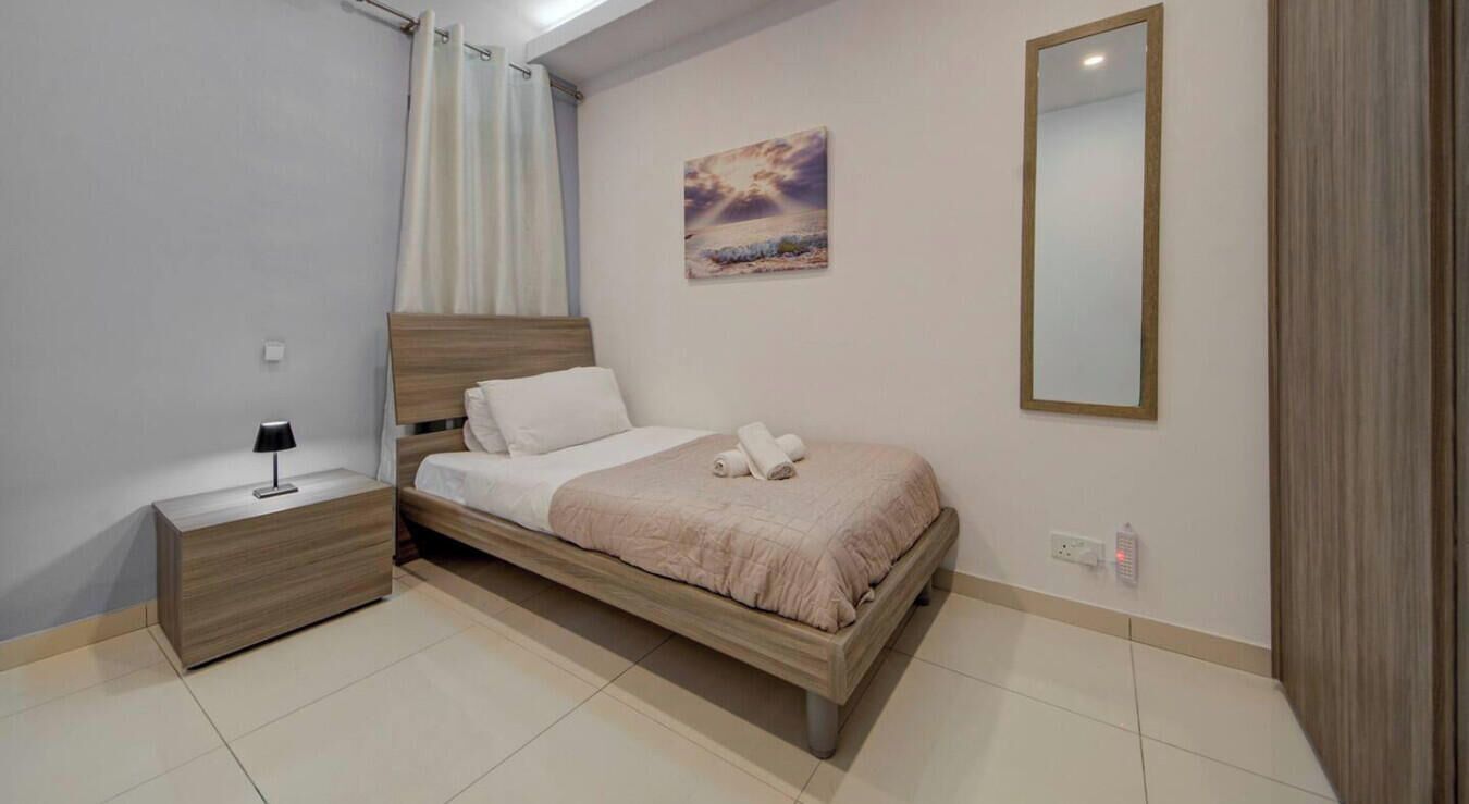 Un dormitorio con cama, mesita de noche, lámpara y un cuadro en la pared.