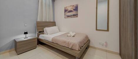 Un dormitorio con cama, mesita de noche, lámpara y un cuadro en la pared.