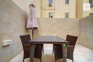 A small outdoor patio with a table and wicker chairs, a hanging umbrella, and a stone wall. - Msida 2BR Home Near University w/ Terrace & WiFi (Msida)