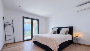 Et soveværelse med seng, et natbord, en lampe, en balkonudgang og et metalstativ.