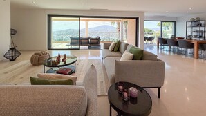 En rummelig opholdsstue med store skydedøre til en balkon, et spiseområde med et træbord og stole, og et hyggeligt siddeområde med sofa og sofabord.