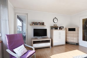 A living room with a TV, a bookshelf, a fireplace, and a chair with a cushion.