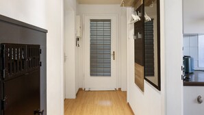Ein Flur mit Holzboden, einer weißen Tür mit Fenster und einem schwarzen Schrank mit Metallgriff.