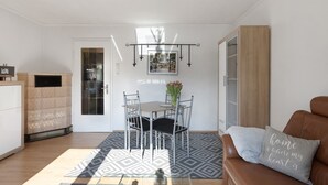 Ein modernes Wohnzimmer mit Essbereich, einem braunen Ledersofa, einem gemusterten Teppich und einem an der Wand hängenden Bild.