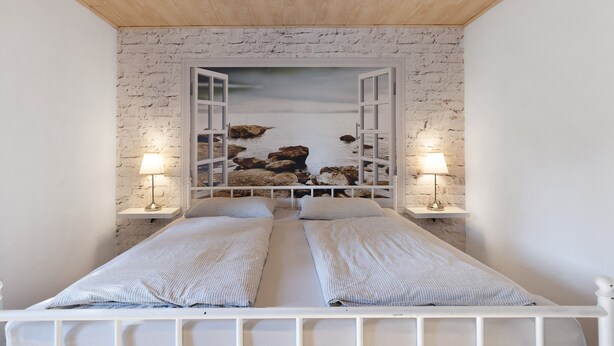 Ein Schlafzimmer mit weißer Ziegelwand, einem Bett mit zwei Kissen und zwei Nachttischlampen.
