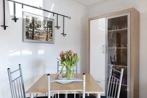 A dining area with a table, chairs, a vase of flowers, a framed picture, and a cabinet.
