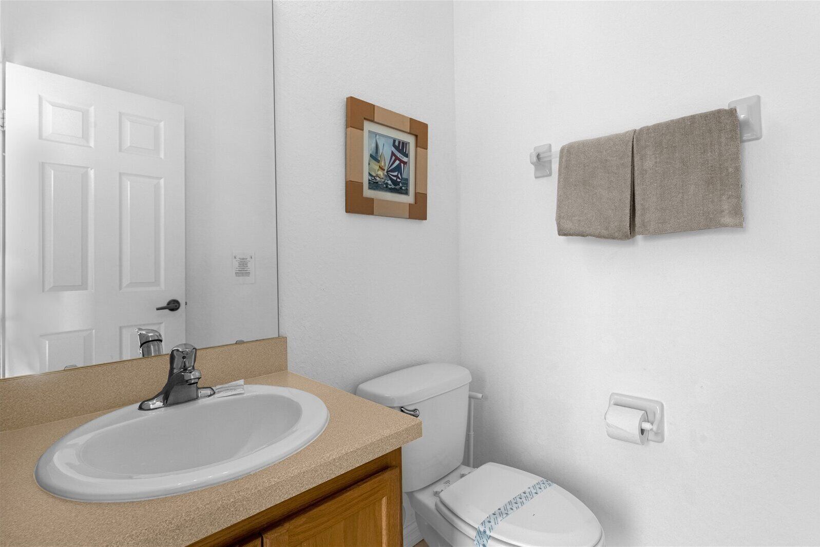 A bathroom with a white sink, a toilet, a towel rack, and a framed picture on the wall.