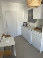 Una cocina compacta con armarios blancos, una encimera blanca, un lavabo, una estufa y una cesta colgante.