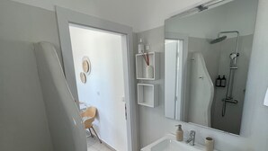 Un baño moderno con lavamanos, espejo y ducha. Hay una puerta que conduce a otra habitación.