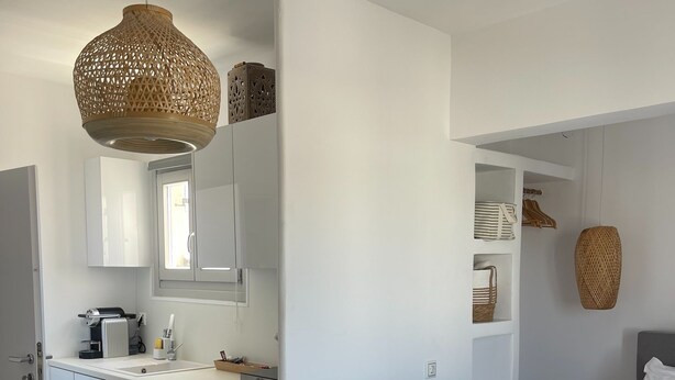 Una habitación de hotel moderna con kitchenette, una cama y toallas ordenadas, y una lámpara colgante tejida.