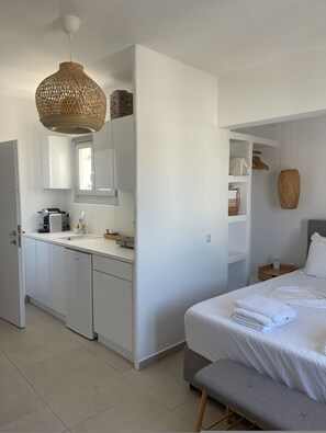 A modern hotel room with a kitchenette, a bed with neatly folded towels, and a hanging woven light fixture. - Chora Nest Kythnos (Kithnos)