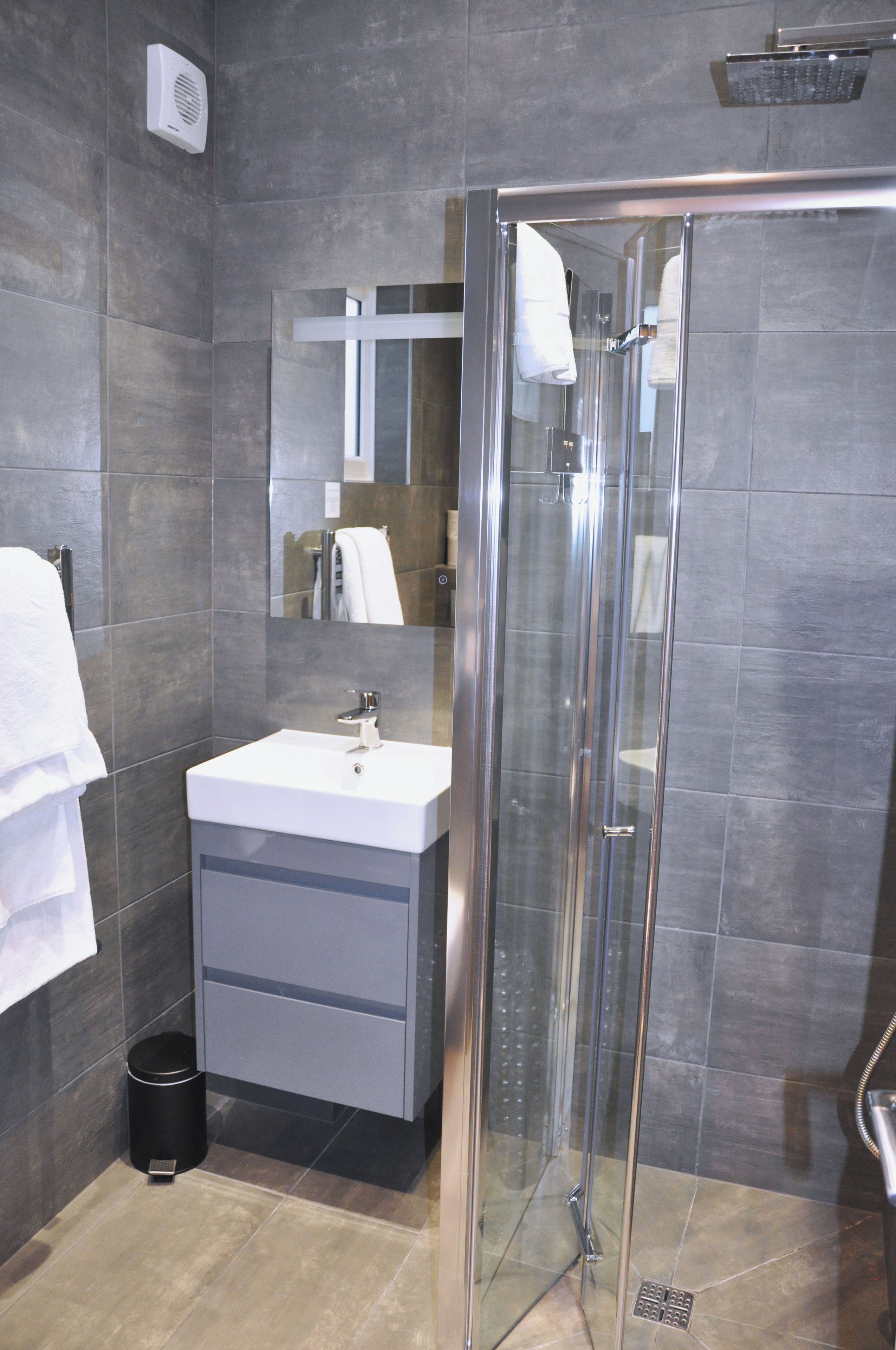 A modern bathroom with a glass shower enclosure, a white sink, and a mirror above it.