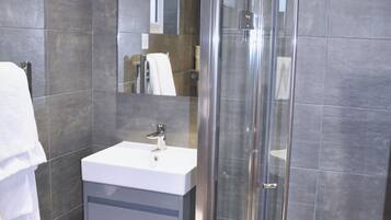 A modern bathroom with a glass shower enclosure, a white sink, and a mirror above it.
