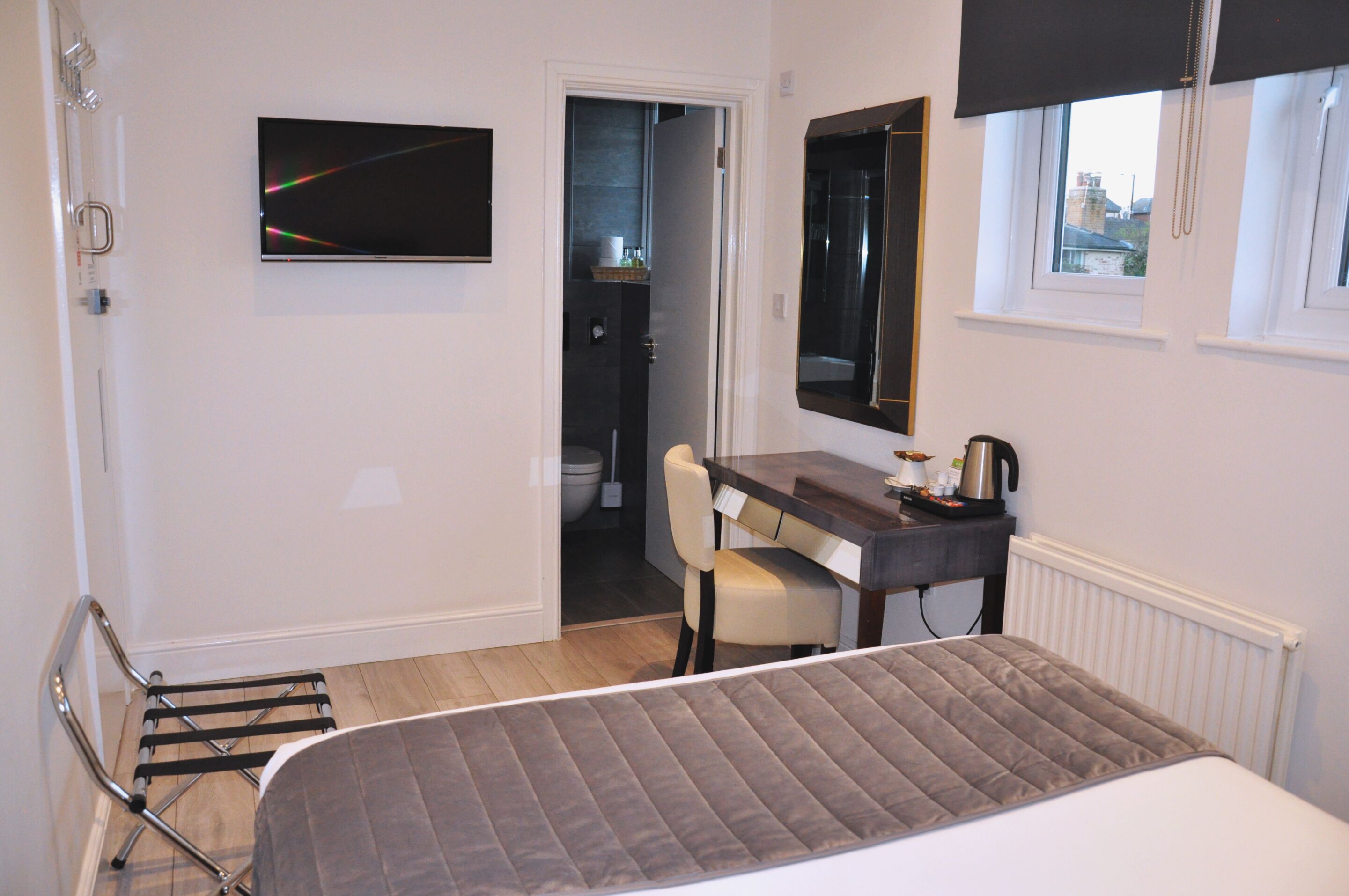 A bedroom with a bed, a desk, a chair, a TV, and a window.