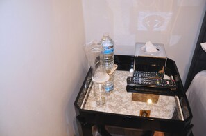 A hotel room with a marble-topped bedside table, a water bottle, a remote control, and a tissue box. - Nap Barnet Hotel (Barnet)