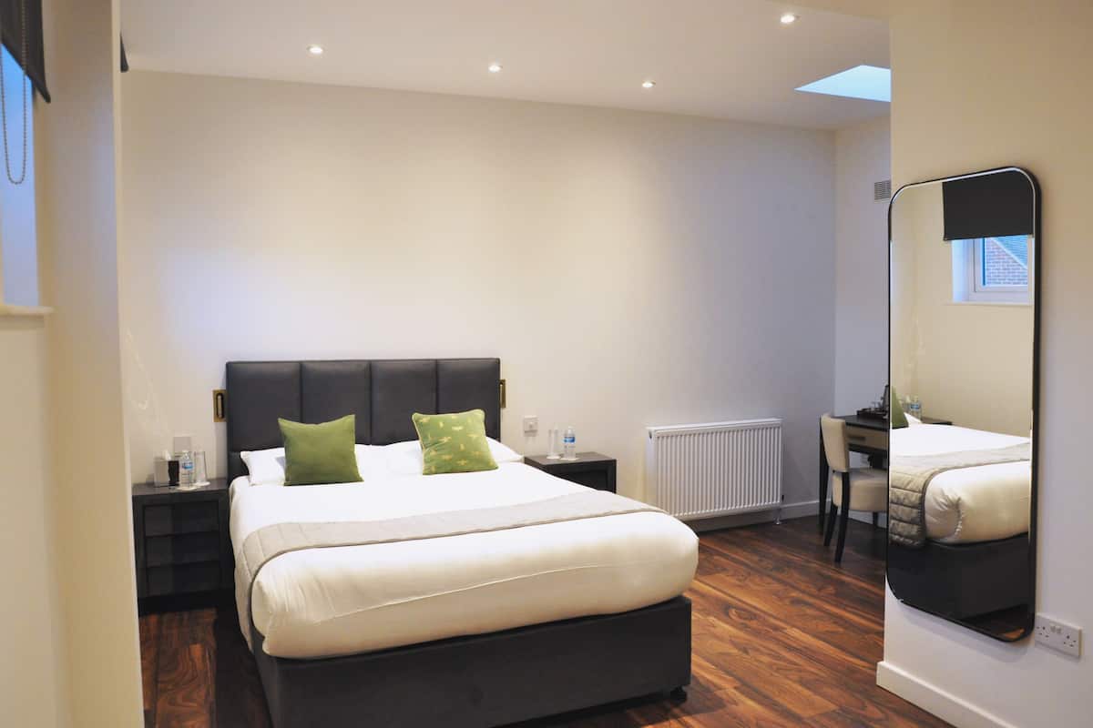 A bedroom with a bed, bedside tables, a desk, and a mirror.