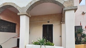 Un edificio con fachada blanca, una puerta con persianas negras y una maceta con plantas verdes.