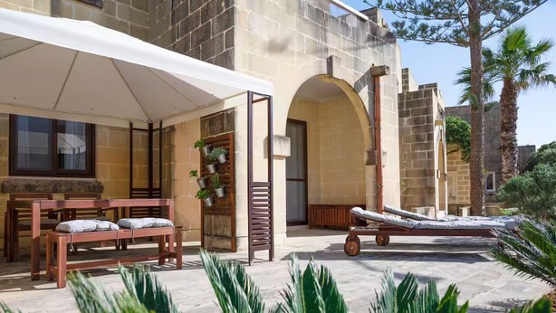 A covered outdoor seating area with a table and chairs, a lounge chair, and potted plants. - Luzzu - Family Friendly Maisonette (Munxar)