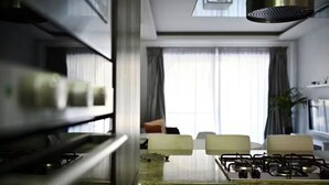 A modern kitchen with a gas stove, a stainless steel range hood, and a view of a living room with a sofa and curtains. - Luzzu - Family Friendly Maisonette (Munxar)