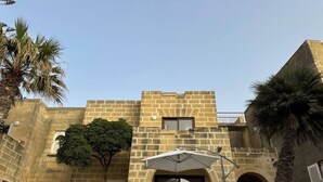 A stone building with a central courtyard, a tree, and a palm tree. - Bizzilla - Family Friendly Maisonette (Munxar)