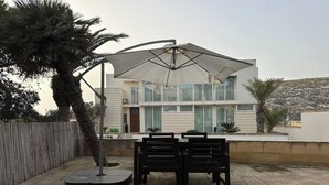 A modern two-story house with a patio area featuring a table and chairs under a large umbrella. - Bizzilla - Family Friendly Maisonette (Munxar)