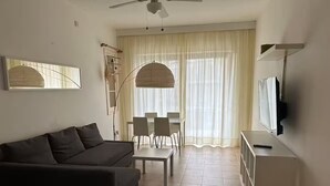 A living room with a sofa, a dining table with chairs, a TV, and a ceiling fan. - Bizzilla - Family Friendly Maisonette (Munxar)