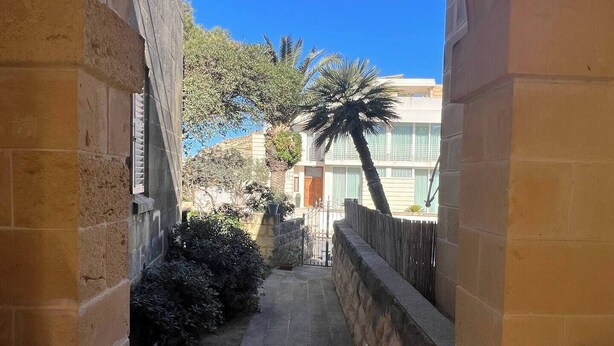 A stone pathway leading to a building entrance framed by an archway. - Bizzilla - Family Friendly Maisonette (Munxar)