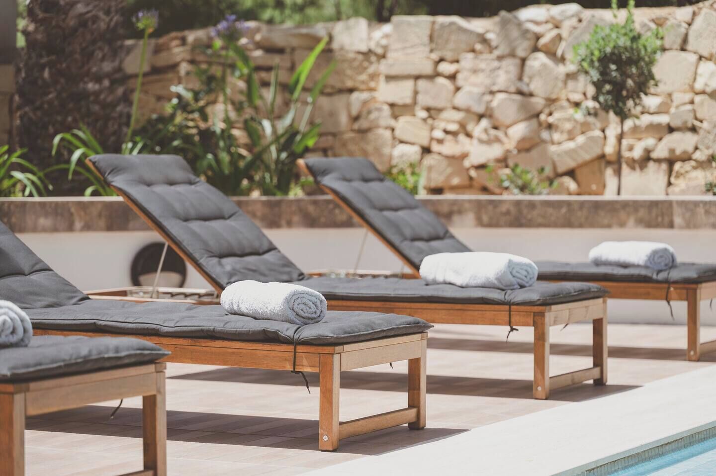 Un espace aménagé au bord de la piscine, avec des chaises longues et un mur de pierre en arrière-plan.