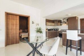 A modern kitchen with wooden cabinets, a glass dining table, and a seating area with a sofa and a plant. - Villa Marni - Luna (Munxar)