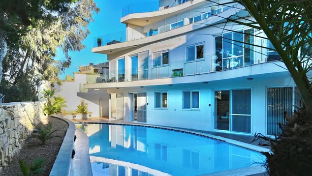 A modern multi-story building with a swimming pool, large windows, and a stone wall. - Villa Marni - Perfume (Munxar)