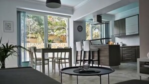 A modern living room with a sofa, dining table, chairs, and a kitchen area with cabinets and a stove. - Villa Marni - Perfume (Munxar)