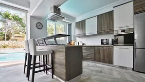 A modern kitchen with a bar area, built-in appliances, and a view of the outdoors. - Villa Marni - Perfume (Munxar)