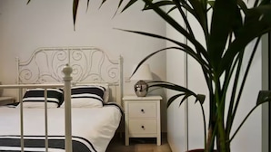 A neatly arranged bedroom with a metal-framed bed, a bedside table with a lamp, and a potted plant. - Luzzu - Family Friendly Maisonette (Munxar)