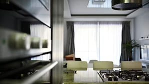 A modern kitchen with a gas stove, a stainless steel range hood, and a view of a living room with a sofa and curtains. - Luzzu - Family Friendly Maisonette (Munxar)