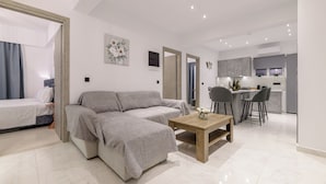 A modern living room with a sofa, a coffee table, and a dining area with chairs. - Athenia Apartments (Zakynthos)