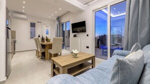 A modern living room with a sofa, a wooden table, and a dining area with chairs. - Athenia Apartments (Zakynthos)