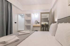 A hotel room with a bed, a desk, a chair, a mirror, and a bathroom visible through an open door. - Athenia Apartments (Zakynthos)