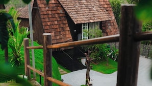 Een landelijke woning met een schuin dak, omringd door weelderige begroeiing en een houten hek.