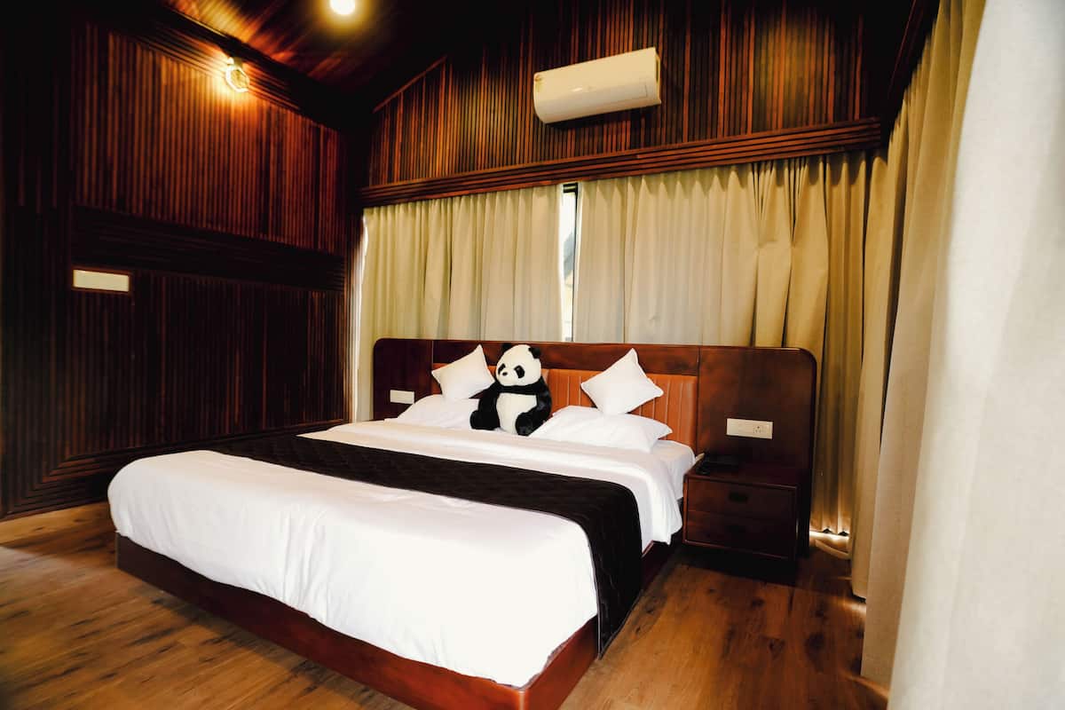 A hotel room with a wooden headboard, a bed with white bedding, a nightstand, and a panda plush toy.